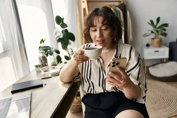 Una mujer joven con el pelo rizado sorbe café mientras se conecta con su teléfono inteligente a la luz del día. — Stock Photo