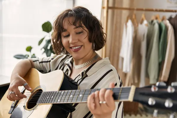 Young woman with curly hair strums a guitar in her stylish apartment during the day. — Stock Photo