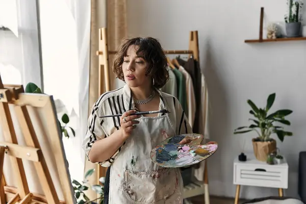 A woman with curly hair paints in her bright, natural-light-filled art space. — Stock Photo