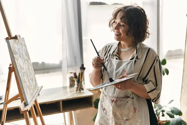 Curly-haired woman immersed in painting, expressing her creativity in a stylish apartment. — Stock Photo