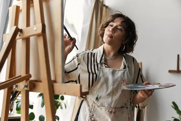 A young woman with curly hair passionately paints at her easel, surrounded by modern decor. — Stock Photo