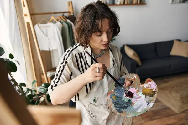 Una joven con el pelo rizado pinta apasionadamente en su elegante apartamento, abrazando la creatividad. — Stock Photo