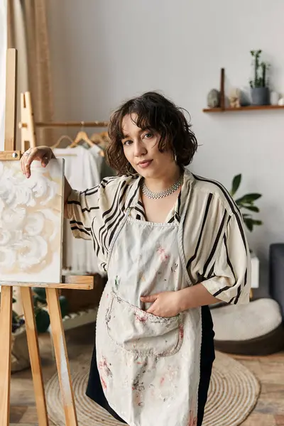 A curly-haired artist paints on an easel in a bright, modern, sunlit apartment. — Stock Photo