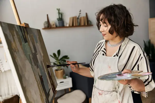 A young woman with curly hair passionately paints on her easel, showcasing her artistic talent. — Stock Photo