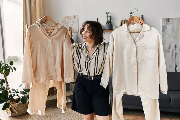 A cheerful young woman holds two outfits, expressing her unique style and personality. — Stock Photo
