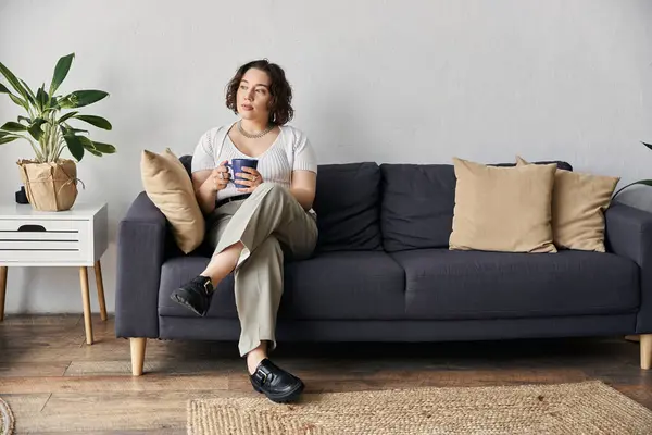 A beautiful young woman relaxes on a couch, sipping a warm drink in her stylish space. — Stock Photo