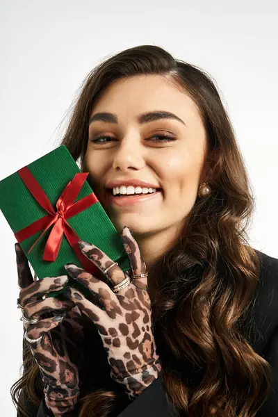 Giovane donna con i capelli lunghi presenta allegramente un regalo avvolto, irradiando felicità e stile. — Foto stock