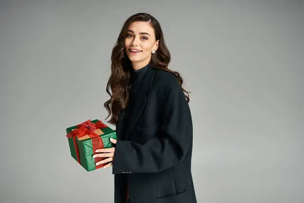 A pretty woman smiles brightly while presenting a colorful gift wrapped in festive paper. — Stock Photo