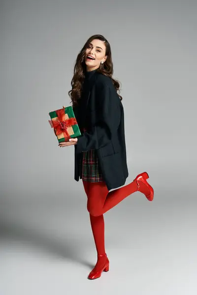 Joyful young woman dressed for the holidays holds a present and plays with her outfit in style — Stock Photo