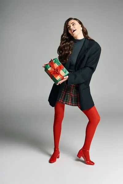Pretty woman in a chic outfit excitedly holds a wrapped present in a studio setting. — Stock Photo