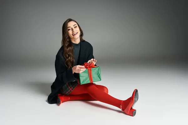 Cheerful young woman with long hair smiles while holding a wrapped gift in a stylish setting. — Stock Photo