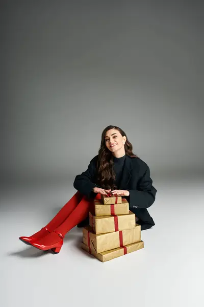 Smiling woman dressed stylishly sits next to elegant presents, exuding holiday cheer. — Stock Photo