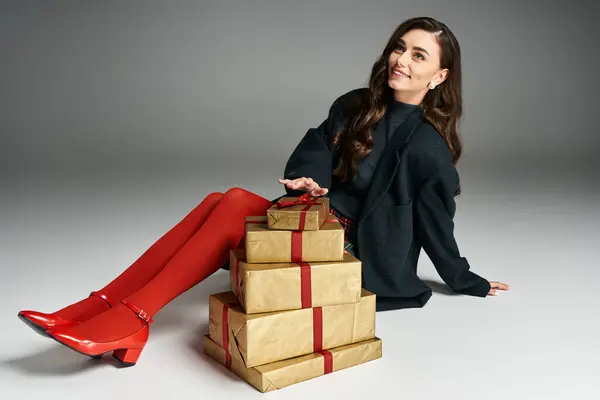 Stylish young woman poses beside beautifully wrapped gifts, enjoying festive moments indoors. — Stock Photo