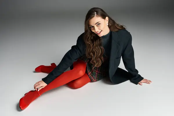 Stylish young woman relaxes gracefully on the floor in a trendy outfit and striking red shoes — Stock Photo