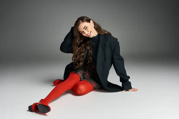 Young woman wearing vibrant colors smiles playfully while sitting on the studio floor. — Stock Photo
