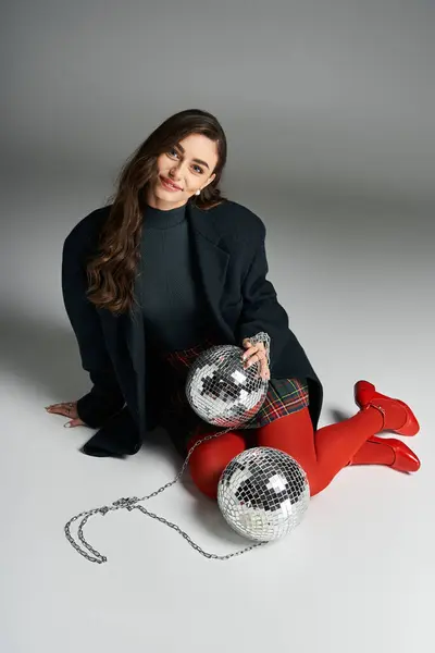 Stylish woman sits comfortably holding disco balls while smiling warmly in a playful pose — Stock Photo
