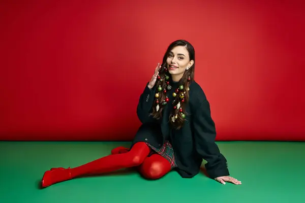Brightly dressed woman happily showcases festive decor against a cheerful red background. — Stock Photo