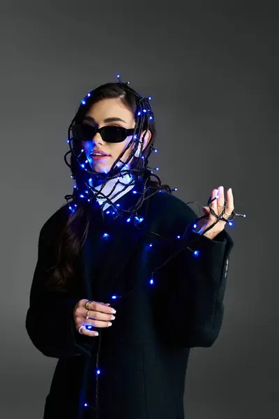 A young woman embraces her style, playfully wrapped in blue fairy lights. — Stock Photo