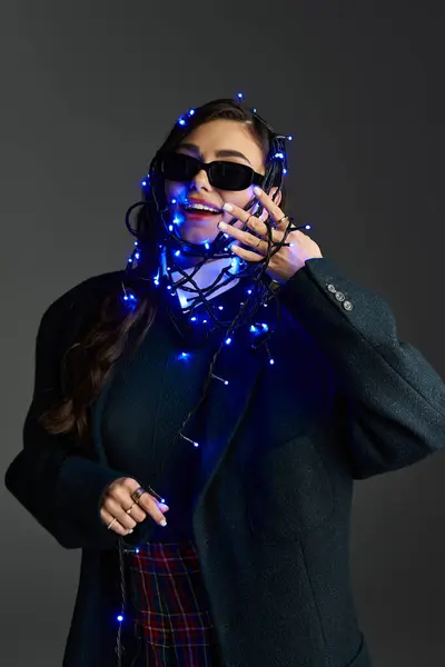 A young woman wrapped in glowing blue lights smiles brightly while posing in a studio. — Stock Photo