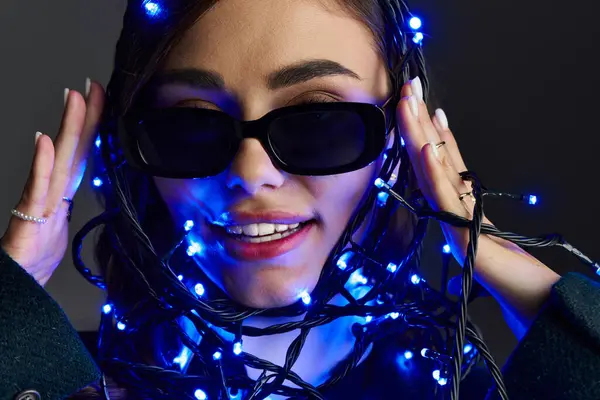 A pretty young woman playfully interacts with shimmering blue lights on a vibrant backdrop. — Stock Photo