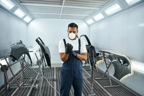 Young man in a workshop checks his gloves before starting his task on car parts — Stock Photo