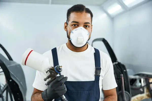 Young mechanic prepares to apply paint with an airbrush in a bright workshop environment. — Stock Photo
