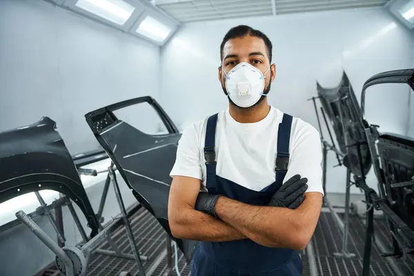 Confident young mechanic in protective gear poses in a well equipped automotive workspace. — Stock Photo