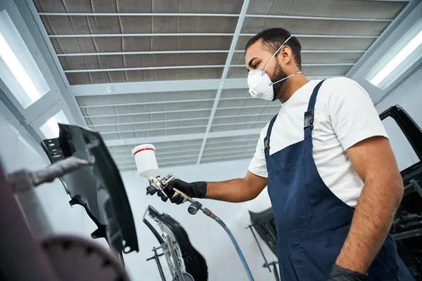 Handsome mechanic applies paint meticulously while wearing protective gear in workshop space. — Stock Photo