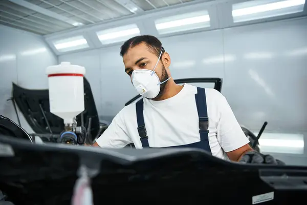 Um jovem mecânico qualificado se concentra em sua tarefa, mantendo a segurança em uma oficina ocupada. — Fotografia de Stock