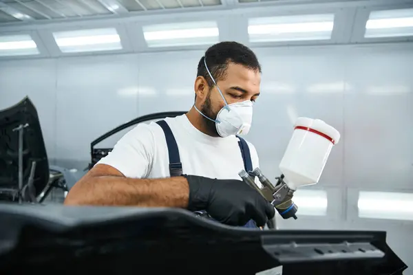 Focused young mechanic applies paint while ensuring precision in an automotive workshop — Stock Photo