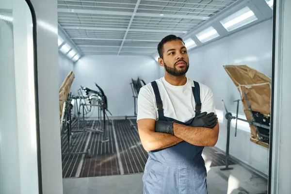 Handsome mechanic wearing gloves poses with confidence in a bright auto workshop. — Stock Photo