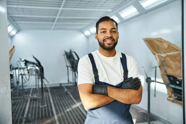 Um jovem mecânico está orgulhosamente com os braços cruzados em uma oficina automotiva bem iluminada. — Stock Photo