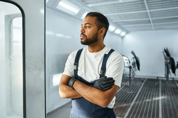 Handsome mechanic stands confidently, thoughts focused on work in a sleek auto repair shop. — Stock Photo