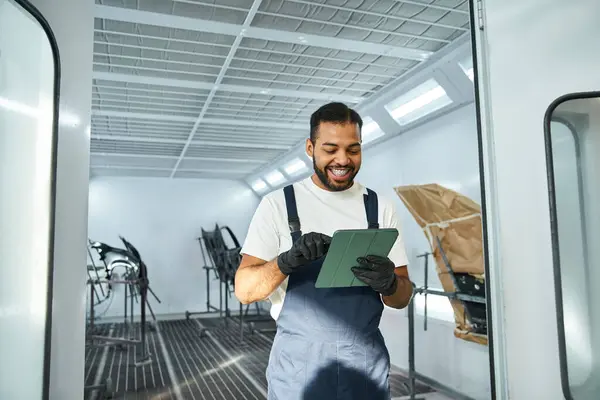 Un mécanicien habile s'engage avec une tablette, souriant dans un environnement de garage propre et bien éclairé. — Photo de stock