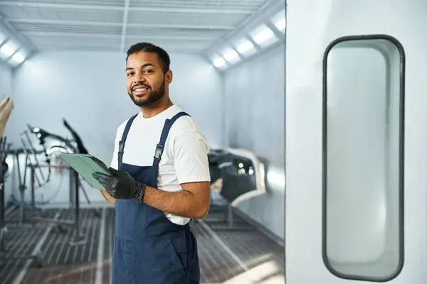 Handsome young mechanic holds a clipboard, showcasing professionalism in a sleek workshop. — Stock Photo