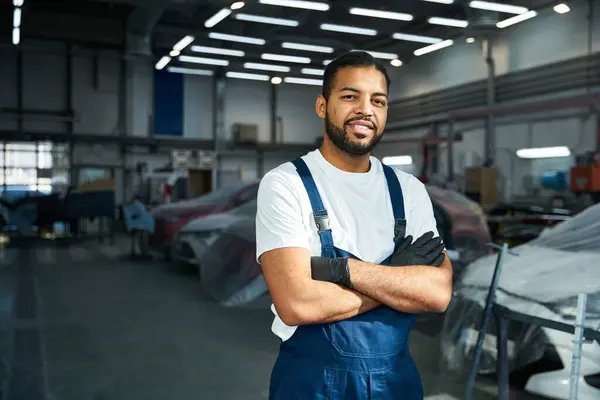 Handsome mechanic stands proud in a vibrant automotive workshop with tools around. — Stock Photo