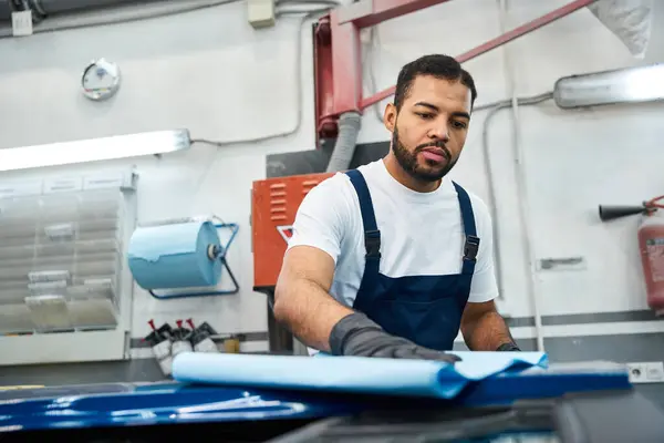 Young mechanic carefully prepares a vehicle surface for maintenance in a bright workshop space. — Stock Photo