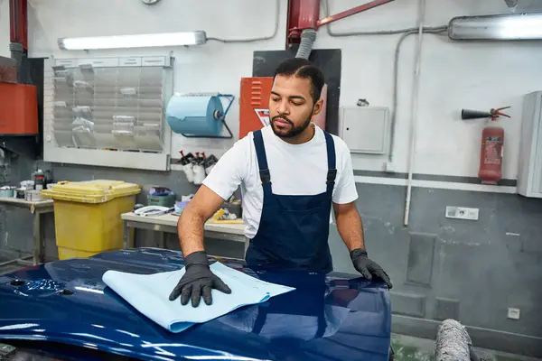 A handsome mechanic works on a blue car part in a tool filled workshop. — Stock Photo