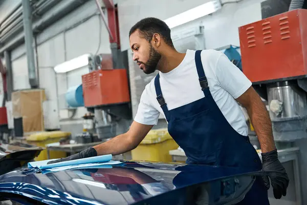 Handsome young mechanic focuses intently on polishing the surface of a car in an auto shop. — Stock Photo