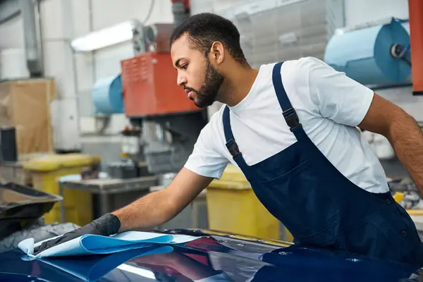 A young mechanic skillfully polishes a car hood in a busy workshop. — Stock Photo