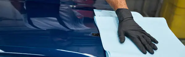 A skilled mechanic wipes a car hood in a bright garage, showing dedication. — Stock Photo