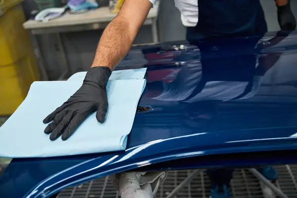 Jeune mécanicien essuie avec diligence un capot de voiture fraîchement peint dans un atelier animé. — Photo de stock