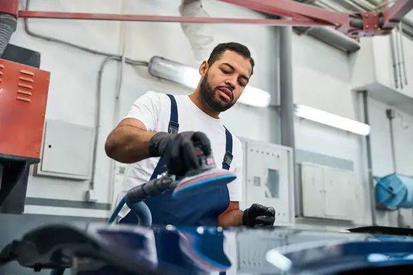 Young and handsome mechanic meticulously refinishing a vehicle in a well equipped garage. — Stock Photo