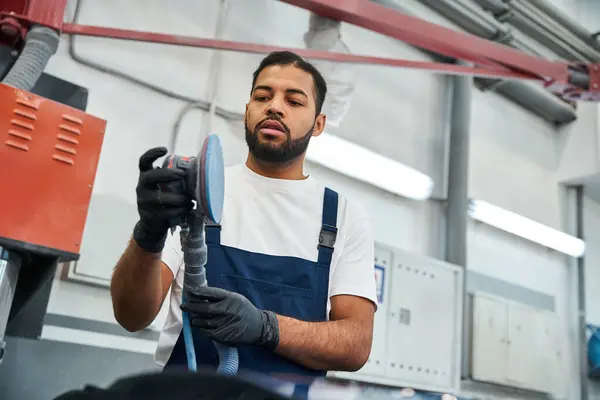 Handsome young mechanic focuses intently while working on a vehicle in a modern garage. — Stock Photo