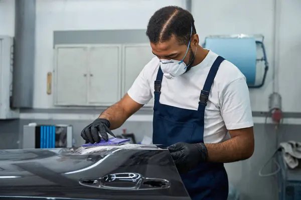 A handsome young mechanic is focused on restoring a vehicles surface with precision and care. — Stock Photo