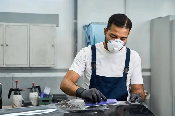 Mechanic in safety gear tackles car repairs in a busy garage. — Stock Photo