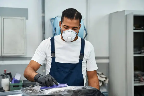 Handsome young mechanic focuses intently while prepping a car for service in a spacious garage. — Stock Photo