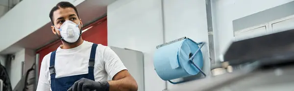 A handsome young mechanic focuses on his task while wearing gloves and a protective mask. — Stock Photo