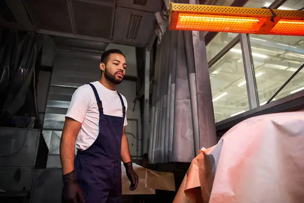 Focused young mechanic inspects equipment under warm overhead lights in a spacious garage. — Stock Photo