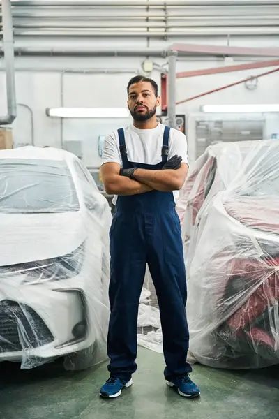 Handsome mechanic stands with arms crossed in a modern garage, showcasing his expertise and style. — Stock Photo